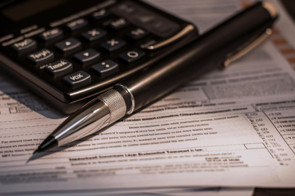 Taxes and pen on a desk: A pen lies on top of a desk, surrounded by paperwork and documents related to taxes.